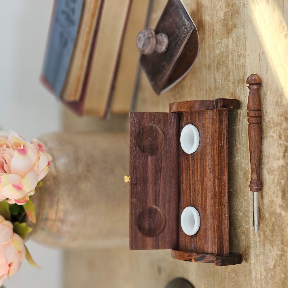 The Inkwell Stand with Porcelain Inkwells and Wood Nib Pen Set makes a perfect desk accessory reminiscent of early Colonial days. The set features a wood inkwell stand that opens and closes, two white porcelain inkwells, a wood nib writing pen, and a bag black ink powder so you can easily get started.