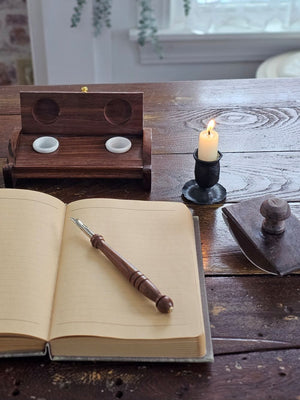 The Inkwell Stand with Porcelain Inkwells and Wood Nib Pen Set makes a perfect desk accessory reminiscent of early Colonial days. The set features a wood inkwell stand that opens and closes, two white porcelain inkwells, a wood nib writing pen, and a bag black ink powder so you can easily get started.