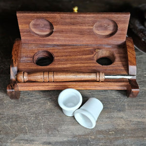 The Inkwell Stand with Porcelain Inkwells and Wood Nib Pen Set makes a perfect desk accessory reminiscent of early Colonial days. The set features a wood inkwell stand that opens and closes, two white porcelain inkwells, a wood nib writing pen, and a bag black ink powder so you can easily get started.