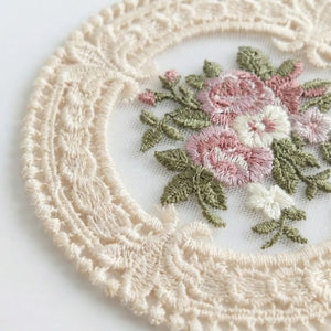 The Lace Embroidered Floral Coaster Set adds timeless elegance to coffee tables, vanities, and dining spaces. Designed with intricate lace detailing and a delicate floral embroidered center, this decorative coaster brings vintage-inspired charm to your home. The fabric construction helps absorb light condensation while providing a soft barrier between cups and surfaces. Ideal for everyday use or display, it combines romantic detailing with practical table protection. Set of four. 4.75" Diam