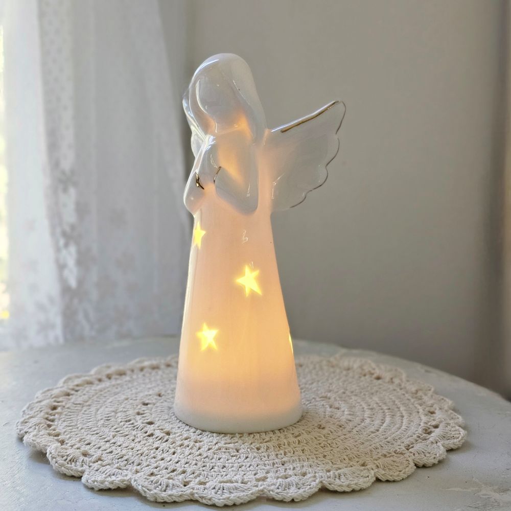 Enhance your home with the serene charm of our Lighted Ceramic Angel. Featuring a simple, organic design, this tabletop piece exudes understated elegance. Its clean white finish remains striking even without the gentle glow of the warm LED light, making it an ideal addition to both classic and modern farmhouse interiors. Requires two LR44 batteries (included). 6.25"H