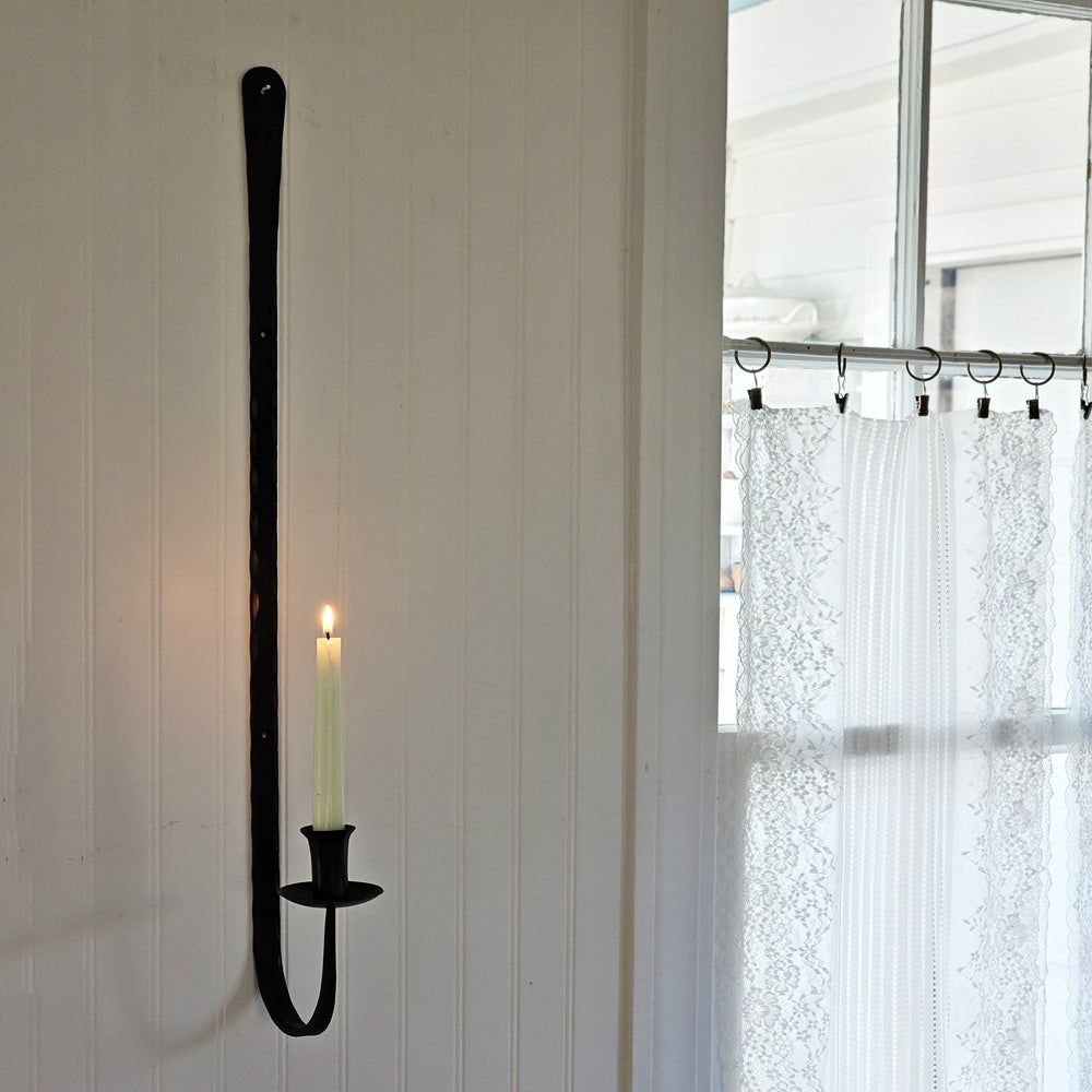 Our rustic taper candle holder looks as though it was hand-forged at an old blacksmith shop from the 1800s. This slender, forged iron wall sconce brings the charming flicker of candlelight to the most unassuming spaces. The Blacksmith Long Iron Taper Candle Sconce mounts with 2 screws, not included. 6.50W x 28"H