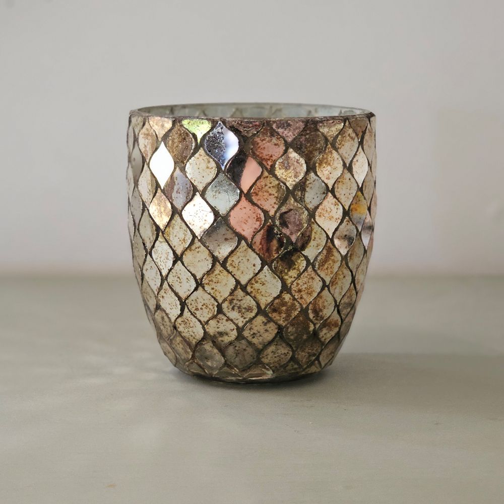 Add a bit of magical ambiance with our Mercury Glass Mosaic Candle Holder. Features aged mirrored glass that sparkles with silver, rose and golden hues. The mirrored glass also picks up the hues of the room decor, making this piece blend in effortlessly with its surroundings. The shimmering glow of candlelight through the cut pattern is dreamy. Can also be used a vase. 4" Diam x 4"H