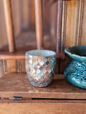 Add a bit of magical ambiance with our Mercury Glass Mosaic Candle Holder. Features aged mirrored glass that sparkles with silver, rose and golden hues. The mirrored glass also picks up the hues of the room decor, making this piece blend in effortlessly with its surroundings. The shimmering glow of candlelight through the cut pattern is dreamy. Can also be used a vase. 4" Diam x 4"H