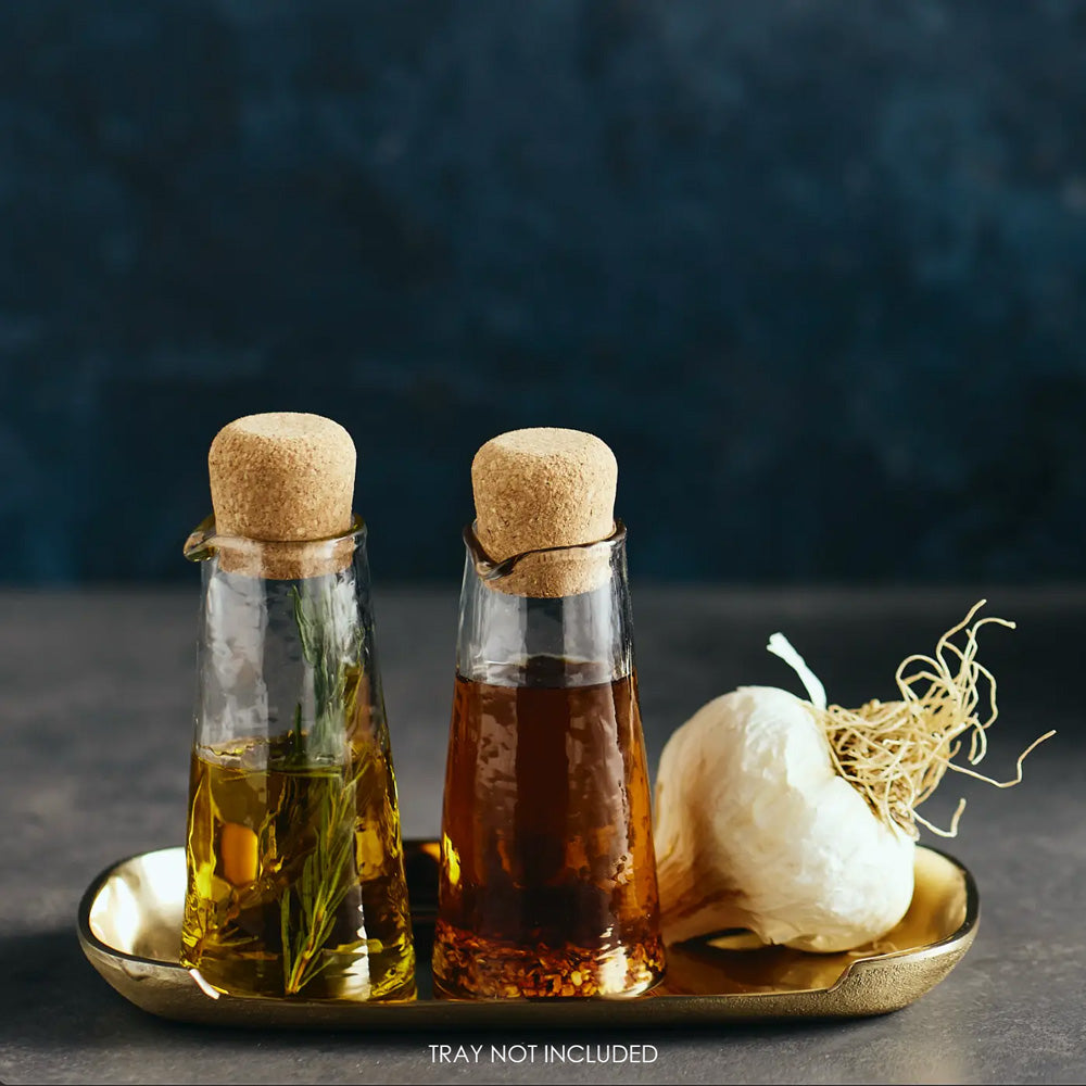 This Mini Glass Cruet, Set of Two, is a perfect choice for personalized servings of oil and vinegar, cream and milk, syrups, and more. Its petite size adds a sweet touch to your place settings. Beyond the kitchen, these charming vessels also serve beautifully as containers for your favorite bath oils or potions, offering a thoughtful touch of refinement wherever they’re placed. The gently pebbled glass surface enhances grip and visual appeal, making these carafes as practical as they are graceful. 