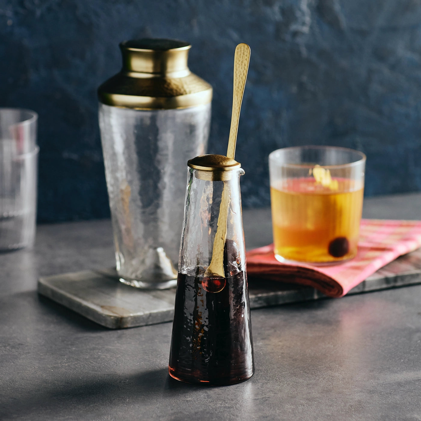 The Mini Glass Carafe with Gold Spoon makes the perfect addition to your kitchen or cocktail bar. With its elegantly tapered body and thoughtfully designed spout, the gently hammered Mini Carafe combines form and function in seamless harmony. Crafted to facilitate effortless drink preparation and serving, it is accompanied by a slender brass spoon that complements the carafe’s refined texture and finish. ideal for serving infused waters, cocktails, or artisanal beverages