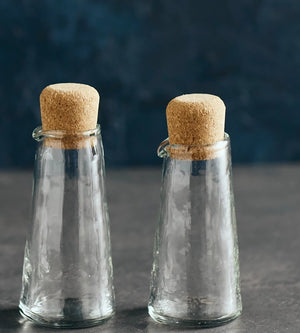 This Mini Glass Cruet, Set of Two, is a perfect choice for personalized servings of oil and vinegar, cream and milk, syrups, and more. Its petite size adds a sweet touch to your place settings. Beyond the kitchen, these charming vessels also serve beautifully as containers for your favorite bath oils or potions, offering a thoughtful touch of refinement wherever they’re placed. The gently pebbled glass surface enhances grip and visual appeal, making these carafes as practical as they are graceful. Each feat