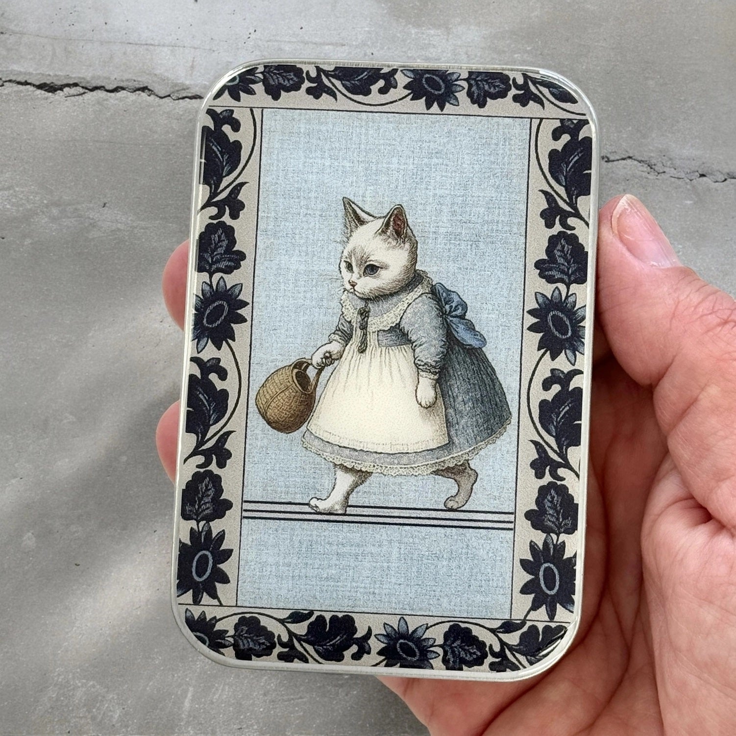 Our Miss Kitty Tin Box has a Beatrix Potter vibe that blends practicality with nostalgia. This delightful tin features a whimsical illustration of THE CUTEST little cat dressed in vintage clothes. The Miss Kitty Tin Box is perfect for storing small items, such as knitting notions, purse essentials and more.&nbsp; This handcrafted box clicks closed and stays closed in any travel bag!&nbsp;3 9/16" length 2 5/16" width 7/16" deep