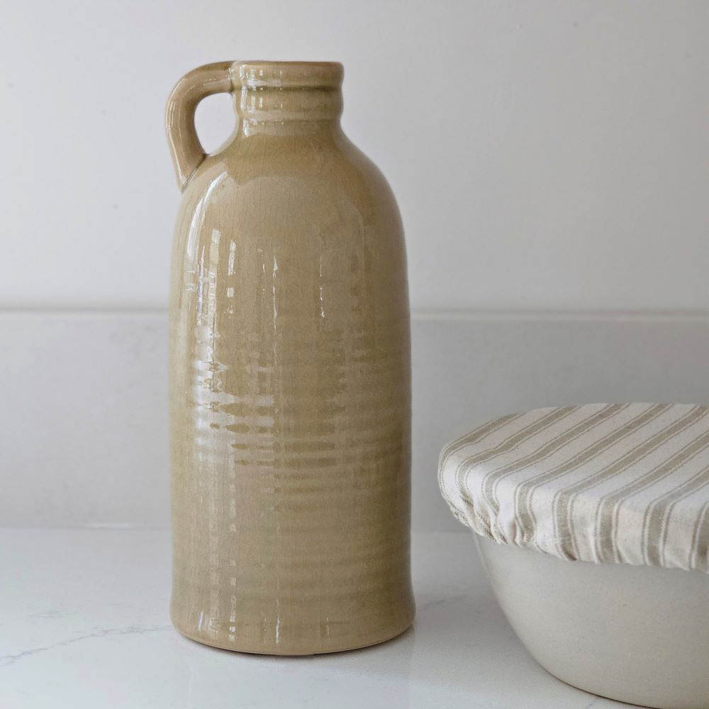 Introduce a touch of Colonial charm to any space with our Mustard Tan Jug with Handle. Crafted from high-quality porcelain and finished with a subtle crackle glaze, this jug is a versatile addition to your decor. Use it as a standalone piece or fill it with flowers for a lovely accent. 4.75" Diam x 11"H