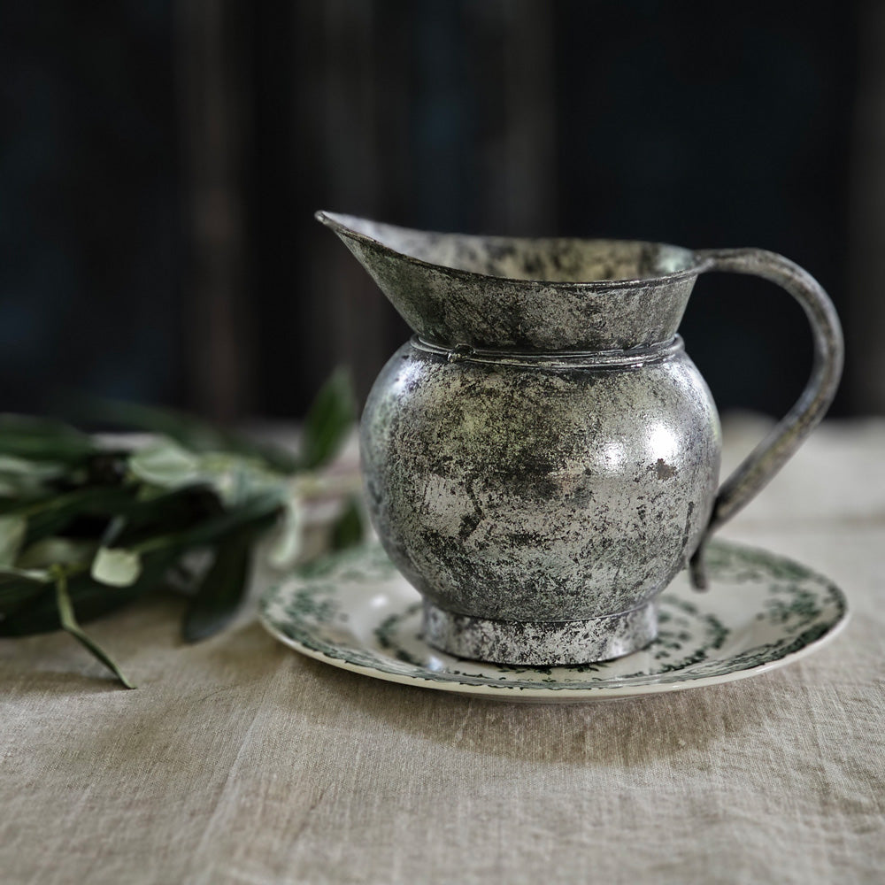 The Old Tarnished Pitcher adds instant character to any shelf or tabletop. This accent piece has an old-world charm that feels timeless and worn. The reproduction silver metal pitcher has an aged finish, making it feel like it has history that spans generations. For decorative use only. 7.5"W (with handle) x 5.75"H