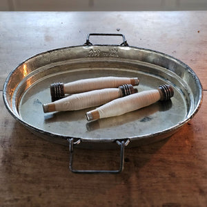 Three spools of thread on Old British Cook Pot Lid tray with handles on a wooden surface.