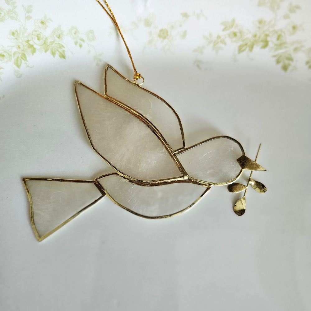 The Peace Dove Ornament, crafted from delicate capiz shell and accented with refined gold plating, adds an enchanted feel to any space. Its translucent glow brings a subtle, captivating charm, making it a graceful addition that enhances any space with a touch of serene elegance. Approximately 4.5"L x 3.5"H