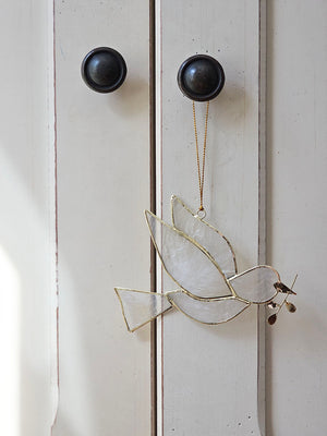 The Peace Dove Ornament, crafted from delicate capiz shell and accented with refined gold plating, adds an enchanted feel to any space. Its translucent glow brings a subtle, captivating charm, making it a graceful addition that enhances any space with a touch of serene elegance. Approximately 4.5"L x 3.5"H