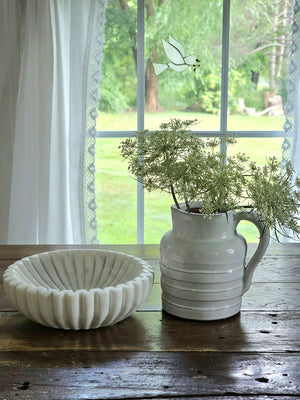The Whitewash Stoneware Ribbed Pitcher offers rustic charm with its simple design. Features a dreamy white glaze over earthy stoneware. Hints of clay tones peek through the ribbed design. It makes the perfect accent for a bedside table, bookshelf or use it as a vase to create a farmhouse centerpiece. 5"Diam x 5"H.