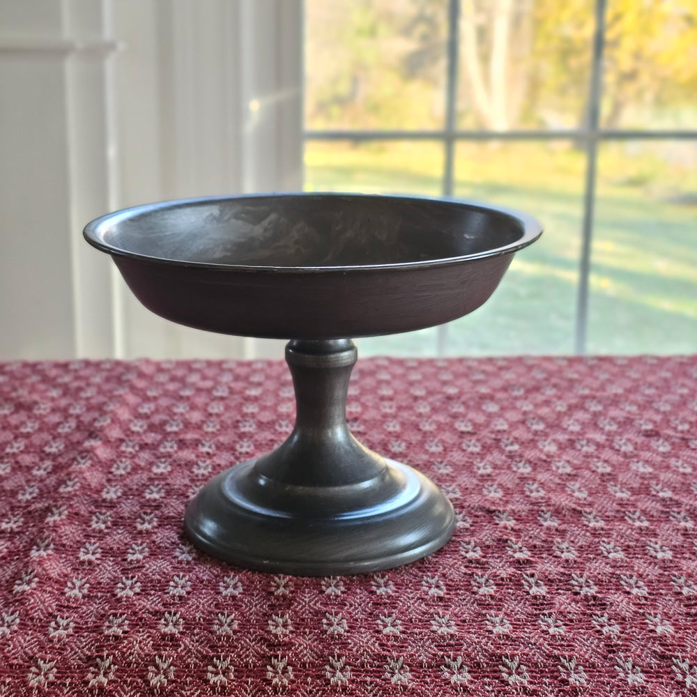 Add an antique touch to any tabletop with our Pewter Style Pedestal Compote. Perfect for displaying candles, holiday bobbles, potpourri and more. This metal pedestal features a pewter look with its aged and lightly distressed grey finish, giving this display riser a timeworn feel. For decorative use only. Candle and Candle Ring not included. 8.25”D x 6”H  