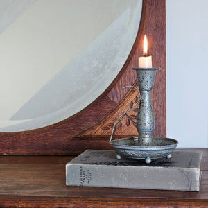 Add an antique touch to any tabletop with our Pewter Style Taper Chamberstick. This metal taper holder features a pewter look with its aged and distressed grey finish, giving this candle holder a timeworn feel. It has an embossed floral design on the tray, a long neck and a graceful handle. Bring Colonial period style to your farmhouse with this charming chamberstick. Candle not included