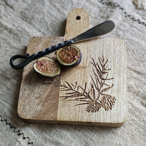 Expertly crafted with a rustic elegance, the Woodland Cutting Board with Iron Spreader is a versatile addition to your kitchen. This small board is perfect for cutting or serving and features an etched pine cone and needles design. The wood cutting board comes with the primitive iron spreader that features a twisted handle design for added rustic charm