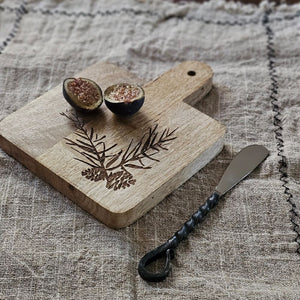 Expertly crafted with a rustic elegance, the Woodland Cutting Board with Iron Spreader is a versatile addition to your kitchen. This small board is perfect for cutting or serving and features an etched pine cone and needles design. The wood cutting board comes with the primitive iron spreader that features a twisted handle design for added rustic charm