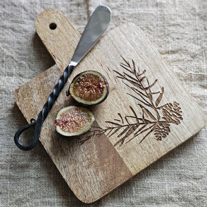 Expertly crafted with a rustic elegance, the Woodland Cutting Board with Iron Spreader is a versatile addition to your kitchen. This small board is perfect for cutting or serving and features an etched pine cone and needles design. The wood cutting board comes with the primitive iron spreader that features a twisted handle design for added rustic charm