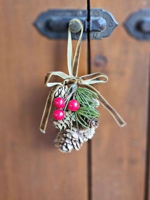 Add a touch of old-fashioned charm to your holiday decor with the Hanging Birchcones and Berries Ornament. Real birchcones beautifully contrast with faux red berries and a pine sprig adorned with a luxurious gold velvet bow. It's the perfect gift topper for a sophisticated and elegant touch. 2.5"W x 3"L