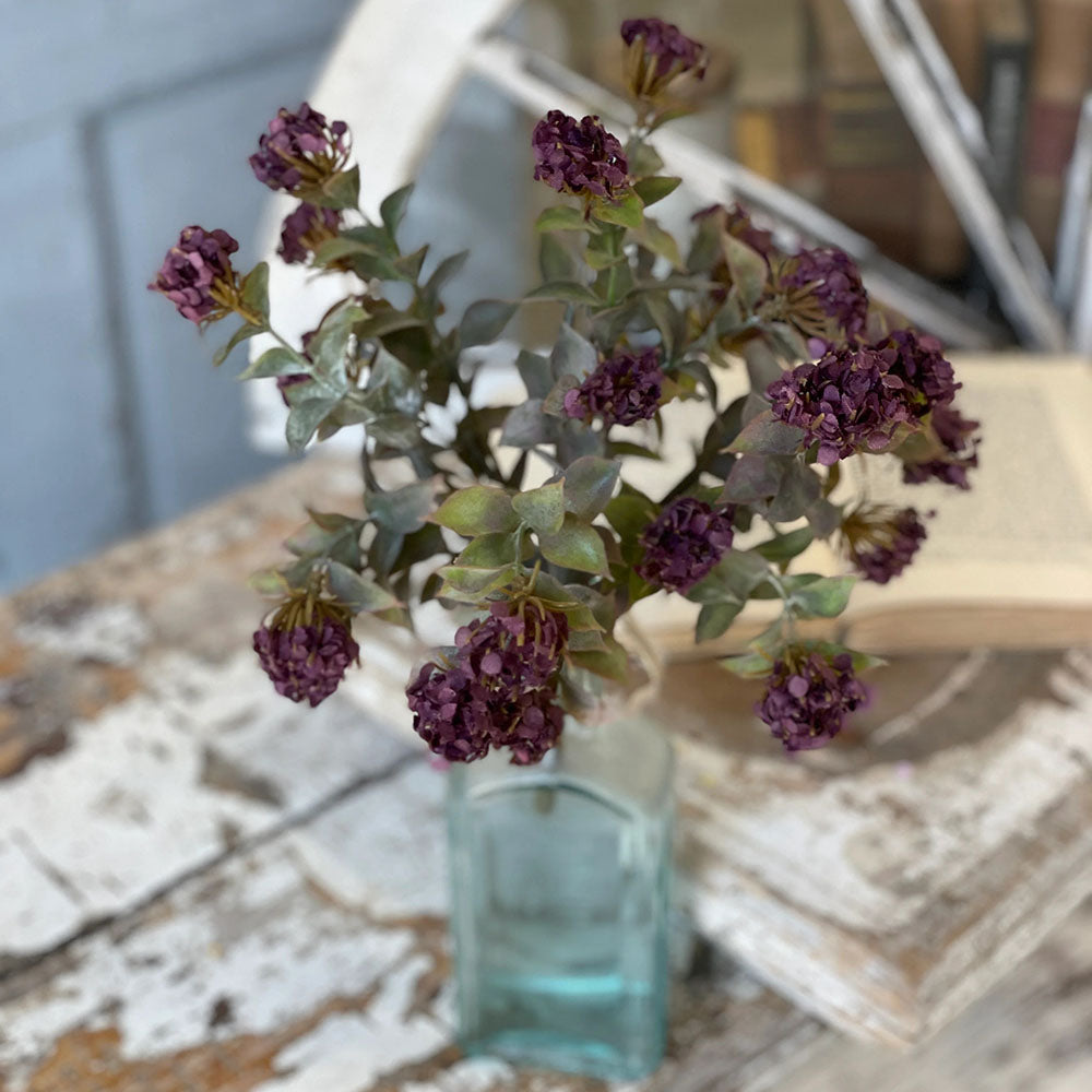 Add rich, moody style to your home with our Plum Colored Blooms Bush. Sweet clusters of plum colored blooms nestle into a bed of green leafy stems. The bush stand 11 inches tall and the deep eggplant color adds old-world beauty to any season. These faux florals will inspire lots of great ideas for any home stylist looking for natural accents without a lot of maintenance. Vase and basket not included. 11” H