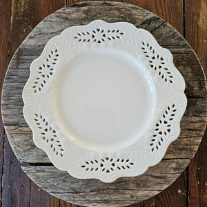 This creamy white porcelain dinner plate marries vintage charm with refined elegance. Featuring hand-detailed embossed flowers and delicate cutout lace work, the gracefully scalloped edge evokes timeless sophistication. Whether gracing your everyday table or reserved for special gatherings, this single plate serves as a subtle statement of cultivated taste and enduring style. Food safe. Microwave safe. Hand wash recommended. Each sold separately. 10" Diam
