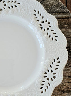 This creamy white porcelain dinner plate marries vintage charm with refined elegance. Featuring hand-detailed embossed flowers and delicate cutout lace work, the gracefully scalloped edge evokes timeless sophistication. Whether gracing your everyday table or reserved for special gatherings, this single plate serves as a subtle statement of cultivated taste and enduring style. Food safe. Microwave safe. Hand wash recommended. Each sold separately. 10" Diam