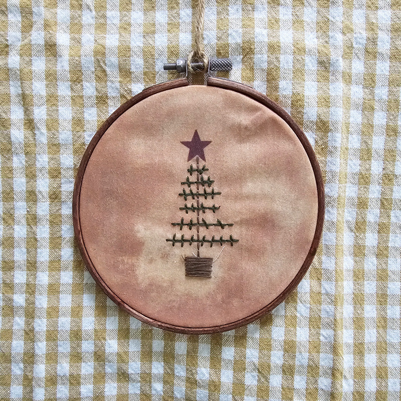 This Primitive Christmas Tree Embroidery Hoop Ornament features a stitched Christmas tree design on an embroidery-style hoop. The old-fashioned stitchery features teastained fabric for an aged finish and its wooden frame is lightly distressed for rustic detail. It has a jute strand for hanging display and measures 5.25" in diameter and .25" deep.