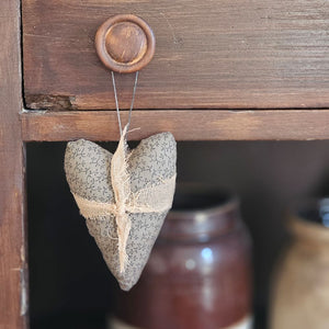 This sweet Primitive Fabric Heart Ornament adds country cottage style all year long. Hang them on a bedroom door as a way to welcome a guest. Pin name tags on them and hang on the back of your dining room chairs as a charming break from traditional place card holders. This primitive heart is a plush pillow, made of antiquated taupe fabric with a simple floral pattern. The heart is adorned with a knotted cheesecloth wrap, as well as a string hanger to use for display.