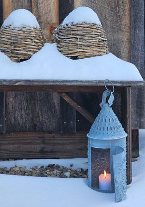 This authentic Colonial reproduction captures the rustic charm of a vintage watchman's lantern with meticulous attention to detail. Crafted from solid metal with a weathered zinc patina, it accommodates a standard 3-inch pillar candle and features an integrated round hook for suspended display or wall mounting. The punched tin design creates a magical glow. 