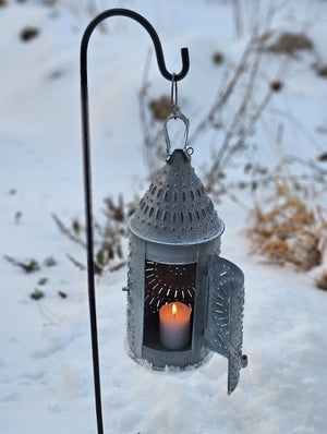 This authentic Colonial reproduction captures the rustic charm of a vintage watchman's lantern with meticulous attention to detail. Crafted from solid metal with a weathered zinc patina, it accommodates a standard 3-inch pillar candle and features an integrated round hook for suspended display or wall mounting. The punched tin design creates a magical glow. 