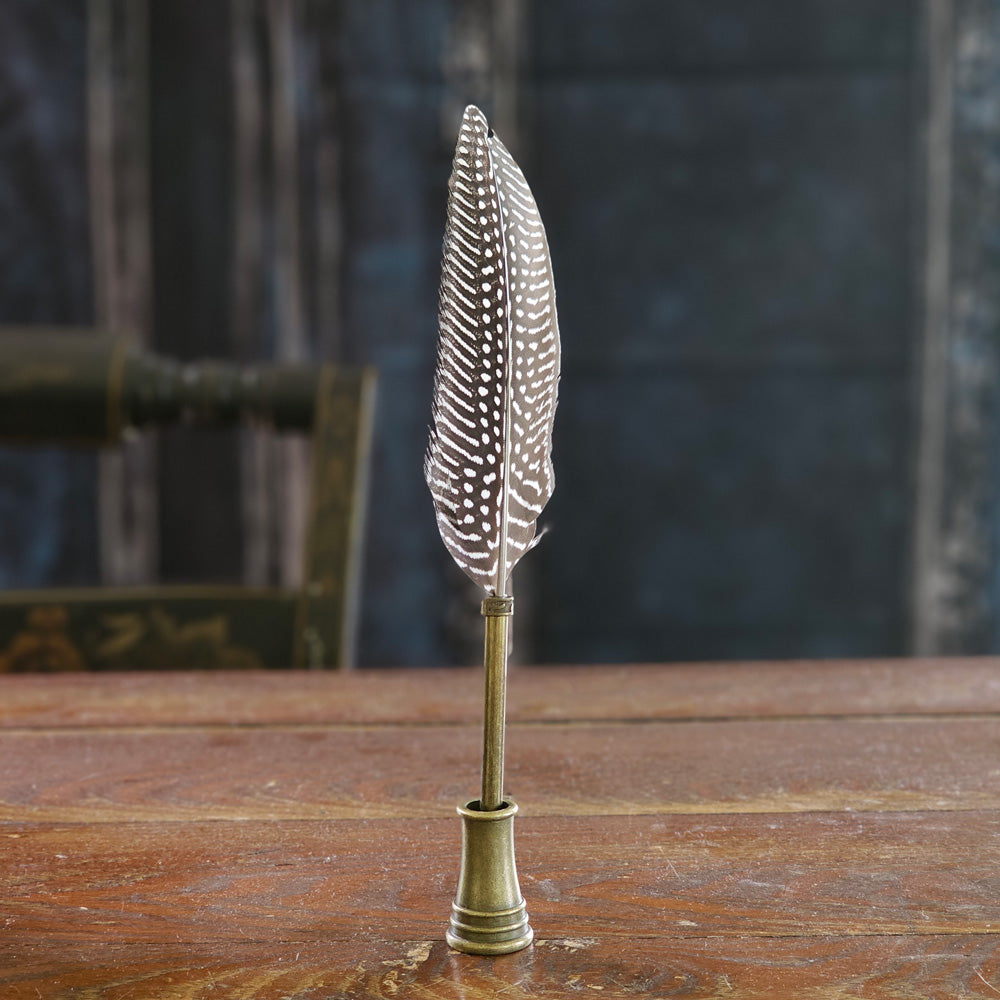 Add antique style to any desk or tabletop with our Quill Pen with Stand. Features a beautifully detailed duck feather with a brass neck on a working ballpoint pen. The stand also has a brass finish for an old-timey touch. It makes a great gift for writers and avid journal keepers. 9"H