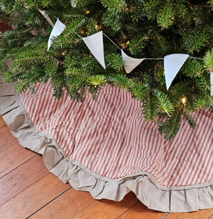 The Red Ticking Stripe Christmas Tree Skirt lends old-timey vintage charm to your holiday home. This 48" regular tree collar has a 100% cotton shell featuring a textured chambray striped pattern and ruffled border for that old-fashioned feel. The reverse side is a rustic farmhouse oatmeal, which gives it a flax linen feel. Wood buttons finish off this beautiful tree skirt.