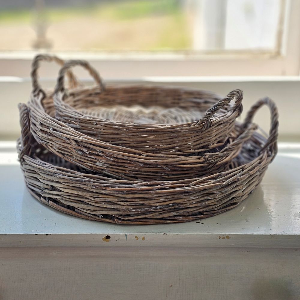 The Round Willow Basket Trays, Set of Three, lends French Country charm to any occasion. The weathered muted grey-tan natural willow has a subtle whitewash finish, giving them a timeless, antique feel. The woven texture adds a rustic, old-world touch. Each has two handles, making them perfect serving trays. Use them as a tabletop accent for a touch of sophistication or hang them on the wall for a rustic look. 