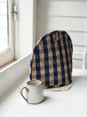 The Rustic Blue Check Tea Cosy is designed to cover your teapot and keep the contents  warm. Its quilted style insulates teapots while also offering English cottage charm to your home. The bold blue and rustic tan buffalo check design create a combination that works with so many decor styles. Whether it's French Country, English cottage or rustic farmhouse, this accent adds a charming touch. 100% Cotton.