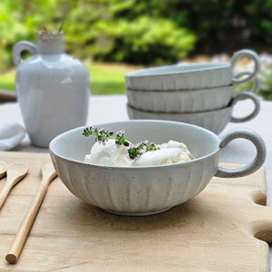 Rustic Ceramic White Bowl with handle keeps a low profile, making it perfect for coffee or soup. Add a candle and it turns into a beautiful chamberstick. This stoneware mug features a white finish speckled with clay tones peaking through the ribbed design. It brings an earthy elegance to your farmhouse kitchen. Each sold separately. Holds approximately 10fl oz. Includes one bowl with handle.