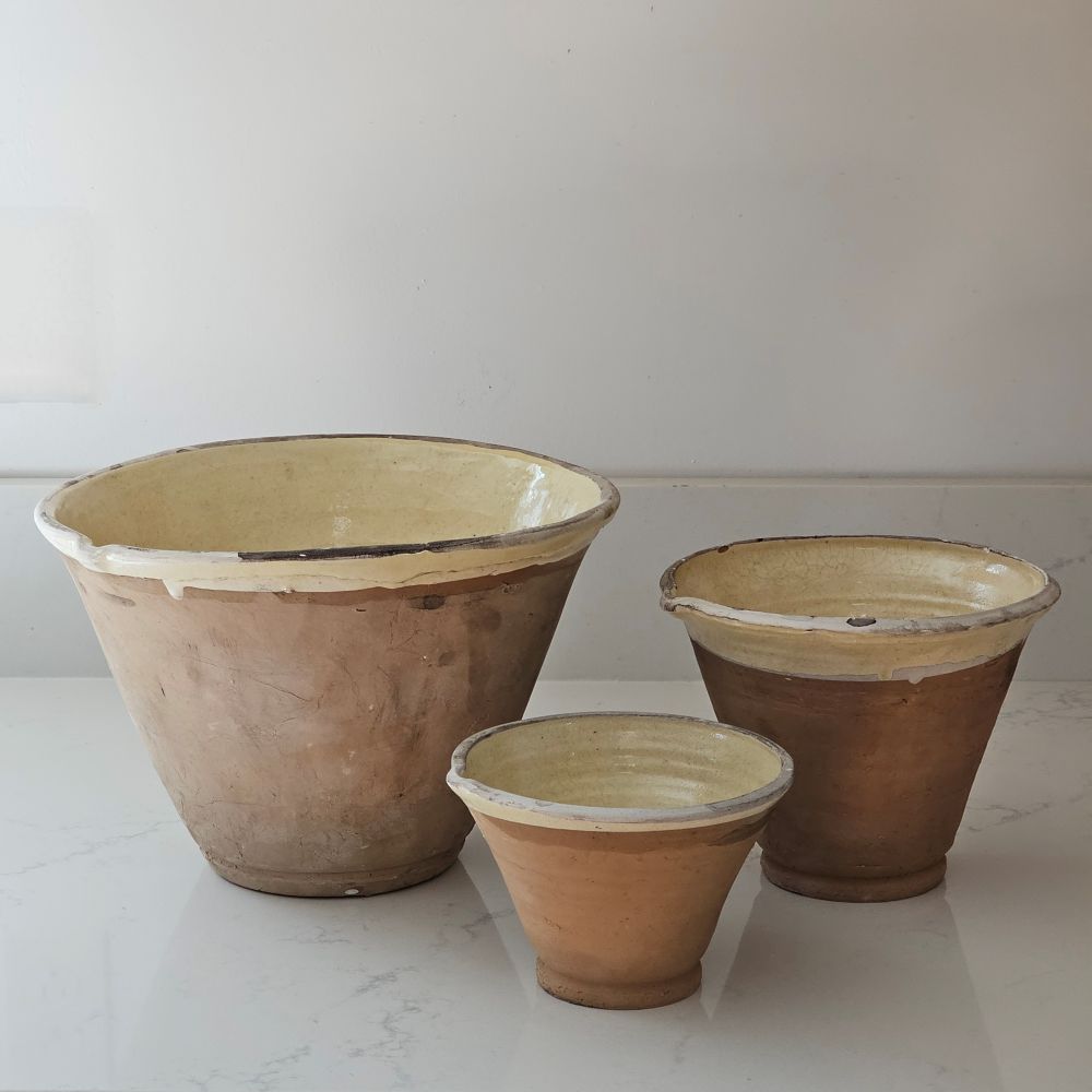 Since the time of the Ancient Greeks, handmade pottery has been a hallmark in southern European farmhouses and beyond. Travel through the Mediterranean regions, and there is no doubt that you will find a bevy of clay dishware. Retaining the rustic, handmade appeal of daily wares, these Rustic Farmhouse Clay Bowls, in three sizes, have a deep, conical shaped basin. The exterior remains a natural clay while the interior and upper lip of the bowl is glazed with a crackled, imperfect buttercream. Set of three