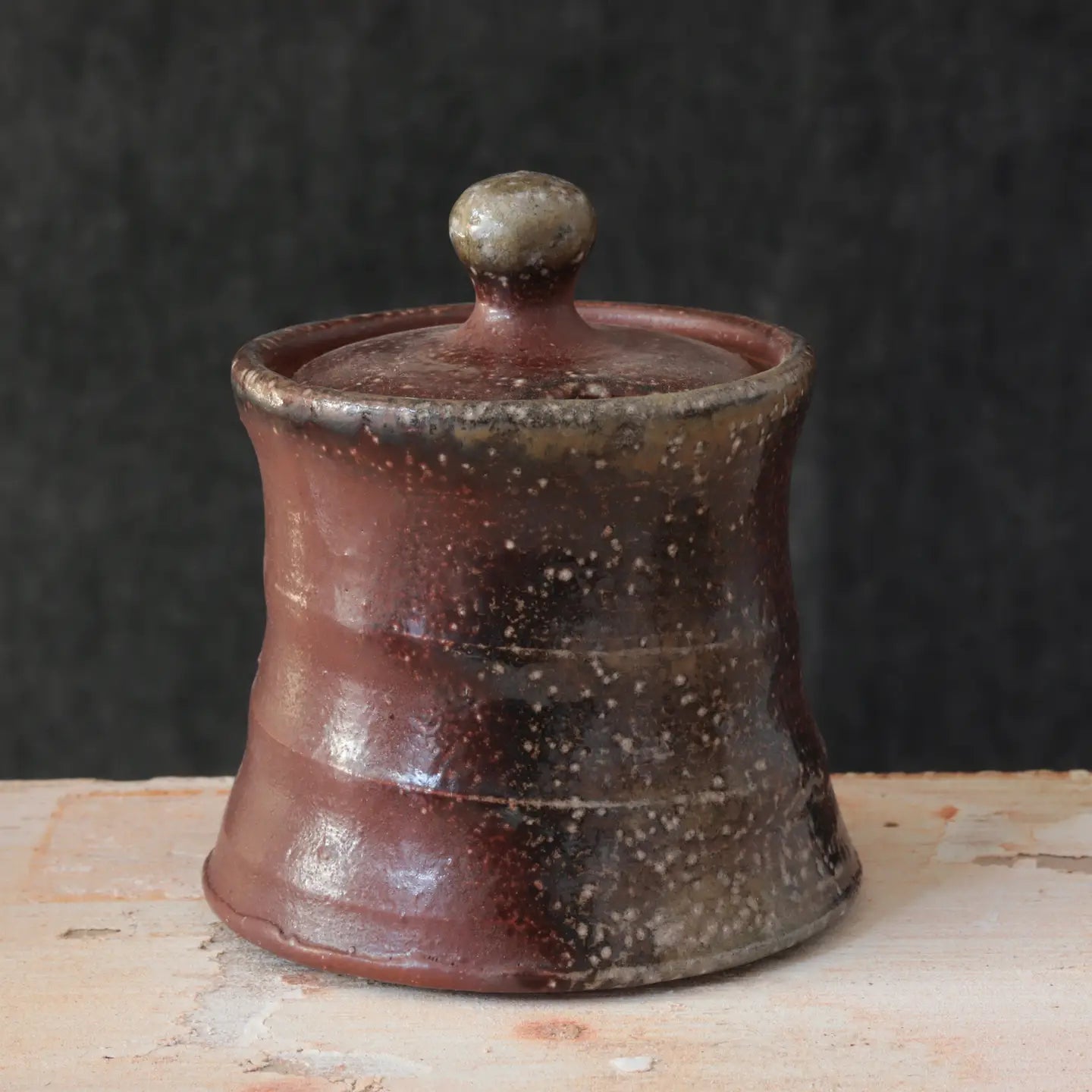 The Rustic Clay Sugar Jar adds instant warmth and texture to your kitchen decor. The clay body is mined and mixed in Northern CA. Various slips made of locally foraged clays, rocks, and wood ash are applied to the pieces before being fired in a soda kiln. Strong reduction (lack of oxygen) from pieces of wood added to the kiln during the firing and cooling help to bring out the various colors and textures of the clay and sips. Made in the USA