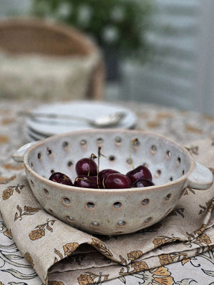 Ceramic colander with cherries on a floral tablecloth