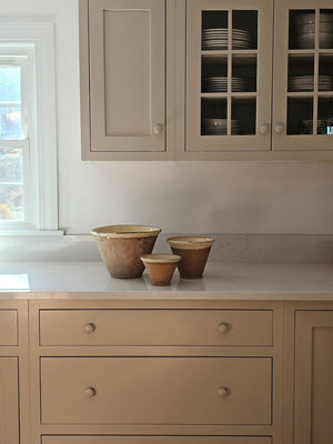 Since the time of the Ancient Greeks, handmade pottery has been a hallmark in southern European farmhouses and beyond. Travel through the Mediterranean regions, and there is no doubt that you will find a bevy of clay dishware. Retaining the rustic, handmade appeal of daily wares, these Rustic Farmhouse Clay Bowls, in three sizes, have a deep, conical shaped basin. The exterior remains a natural clay while the interior and upper lip of the bowl is glazed with a crackled, imperfect buttercream. Set of three