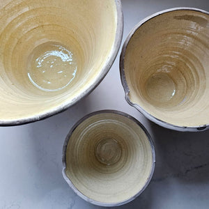 Since the time of the Ancient Greeks, handmade pottery has been a hallmark in southern European farmhouses and beyond. Travel through the Mediterranean regions, and there is no doubt that you will find a bevy of clay dishware. Retaining the rustic, handmade appeal of daily wares, these Rustic Farmhouse Clay Bowls, in three sizes, have a deep, conical shaped basin. The exterior remains a natural clay while the interior and upper lip of the bowl is glazed with a crackled, imperfect buttercream. Set of three