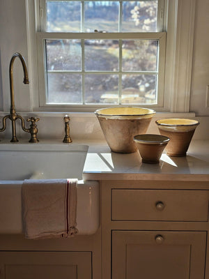 Since the time of the Ancient Greeks, handmade pottery has been a hallmark in southern European farmhouses and beyond. Travel through the Mediterranean regions, and there is no doubt that you will find a bevy of clay dishware. Retaining the rustic, handmade appeal of daily wares, these Rustic Farmhouse Clay Bowls, in three sizes, have a deep, conical shaped basin. The exterior remains a natural clay while the interior and upper lip of the bowl is glazed with a crackled, imperfect buttercream. Set of three