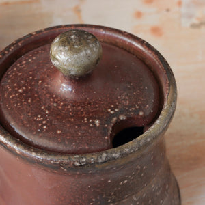 The Rustic Clay Sugar Jar adds instant warmth and texture to your kitchen decor. The clay body is mined and mixed in Northern CA. Various slips made of locally foraged clays, rocks, and wood ash are applied to the pieces before being fired in a soda kiln. Strong reduction (lack of oxygen) from pieces of wood added to the kiln during the firing and cooling help to bring out the various colors and textures of the clay and sips. Made in the USA