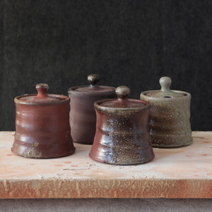 The Rustic Clay Sugar Jar adds instant warmth and texture to your kitchen decor. The clay body is mined and mixed in Northern CA. Various slips made of locally foraged clays, rocks, and wood ash are applied to the pieces before being fired in a soda kiln. Strong reduction (lack of oxygen) from pieces of wood added to the kiln during the firing and cooling help to bring out the various colors and textures of the clay and sips. Made in the USA