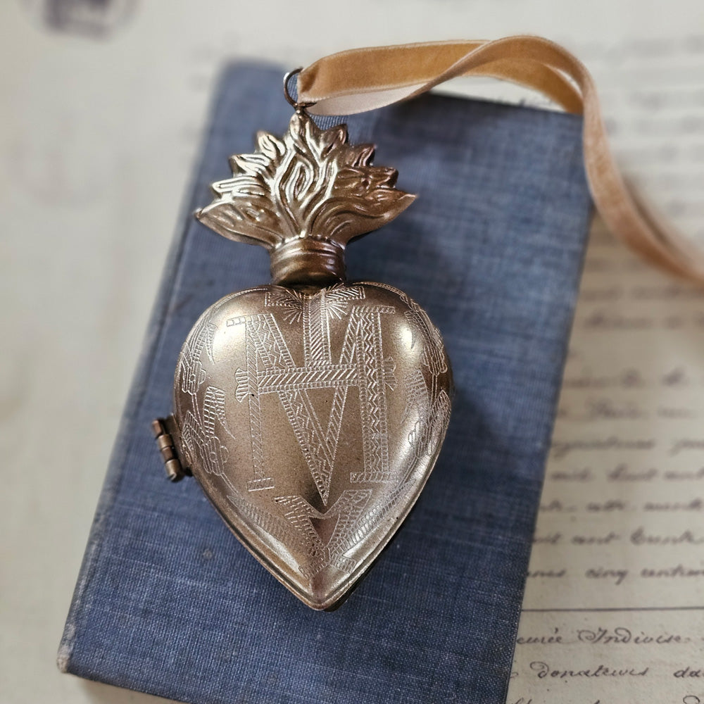 Introducing the Sacred Heart Locket Box, the perfect blend of vintage style and old-world charm. Crafted from aged metal with a golden bronze finish and intricate etchings, this locket box offers a timeless storage solution for your sacred treasures. Hang it from a chain or ribbon with the attached loop (Ribbon not included).