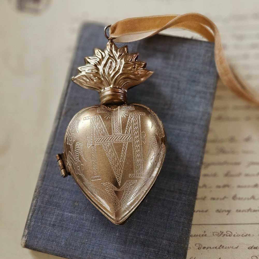 Introducing the Sacred Heart Locket Box, the perfect blend of vintage style and old-world charm. Crafted from aged metal with a golden bronze finish and intricate etchings, this locket box offers a timeless storage solution for your sacred treasures. Hang it from a chain or ribbon with the attached loop (Ribbon not included). A must-have for any collector.&nbsp; Includes one heart locket box. Available in two different sizes. Med: 1.75"W x 3.25"H, Large: 2.5"W x 5"H