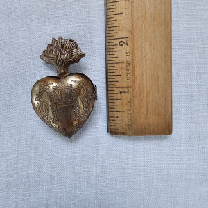 Introducing the Sacred Heart Locket Box, the perfect blend of vintage style and old-world charm. Crafted from aged metal with a golden bronze finish and intricate etchings, this locket box offers a timeless storage solution for your sacred treasures. Hang it from a chain or ribbon with the attached loop (Ribbon not included). A must-have for any collector. 