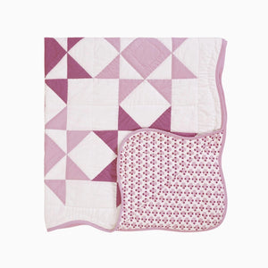 Make this Sweet Sawtooth Star Quilted Throw a treasured heirloom. A fresh take on the iconic sawtooth star quilt block, this organic cotton patchwork throw is hand quilted by skilled artisans. The antique-inspired design features pinkish-lilac and magenta stars with a playful pin dot pattern. Fully reversible, the quilt backing showcases a coordinating floral print. This country classic quilt design is finished with a playful scalloped binding. 