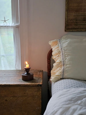 Candle on a wooden nightstand next to a bed with white bedding and a starfish decoration on the window. Scribner Candle Holder and Velvet Ribbon Pillowcase set