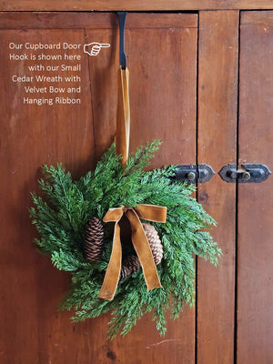 The Small Cedar Wreath with Velvet Bow and Hanging Ribbon adds a refined touch to kitchen cabinets, windows, and cupboards. Crafted with realistic faux cedar foliage and pinecones, it brings understated elegance to any space. Finished with a plush velvet bow and an attached ribbon, this wreath offers effortless and graceful hanging. 13" Diam